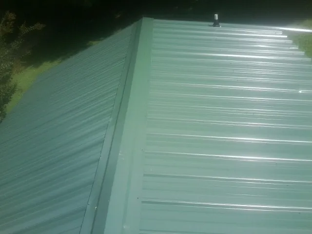 New green metal panels meeting at the ridge of a roof — Flat Roof Repair work by our crew in Knoxville