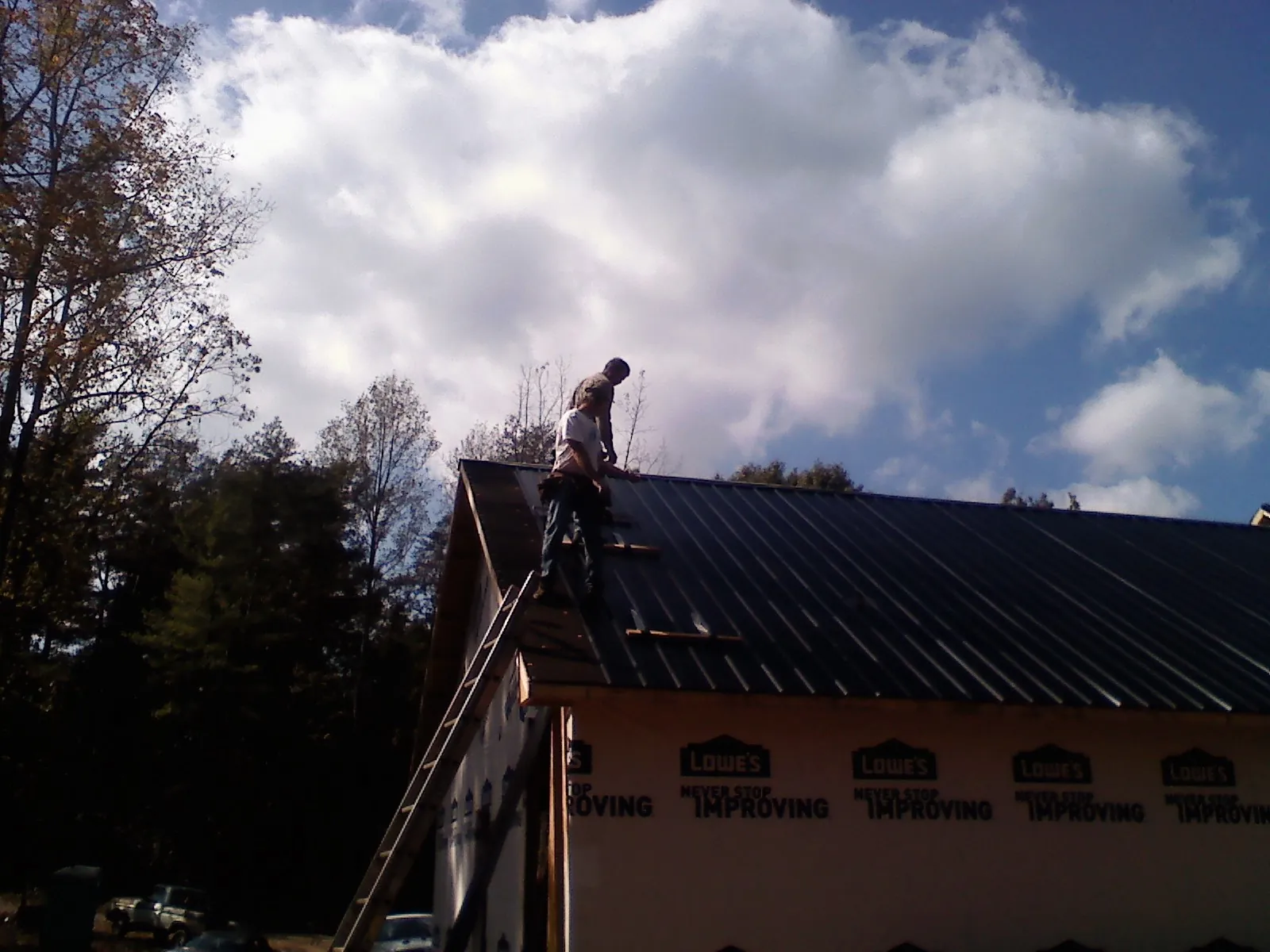 Roofer fastening dark metal panels high against a cloudy sky, from a Roof Inspection job in Knoxville