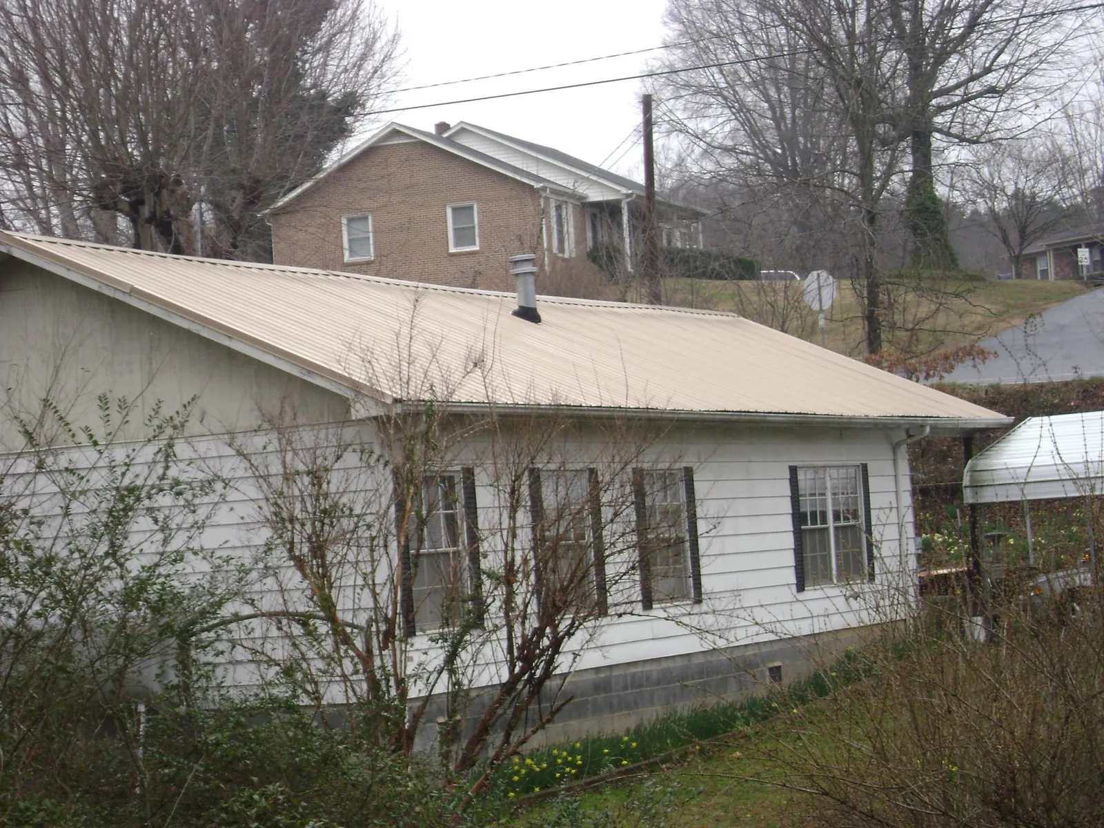 Tan metal roof on a white sided house set into a hillside — Commercial Roofing by Roofing Brothers in Knoxville